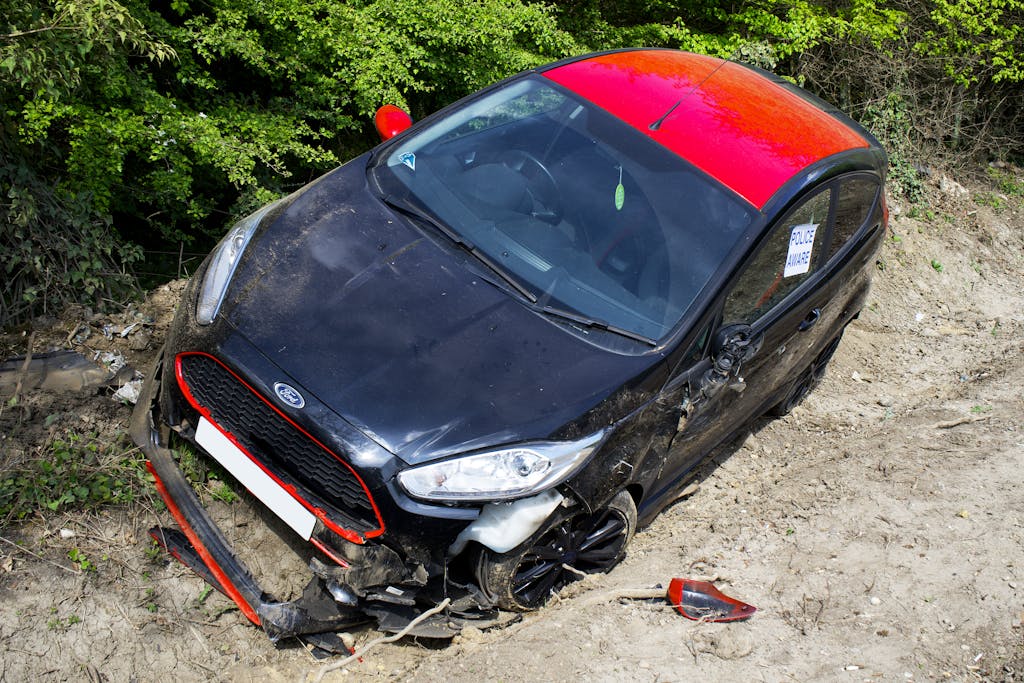 A black and red Ford Fiesta lies abandoned and damaged off-road in Welwyn Garden City, UK.