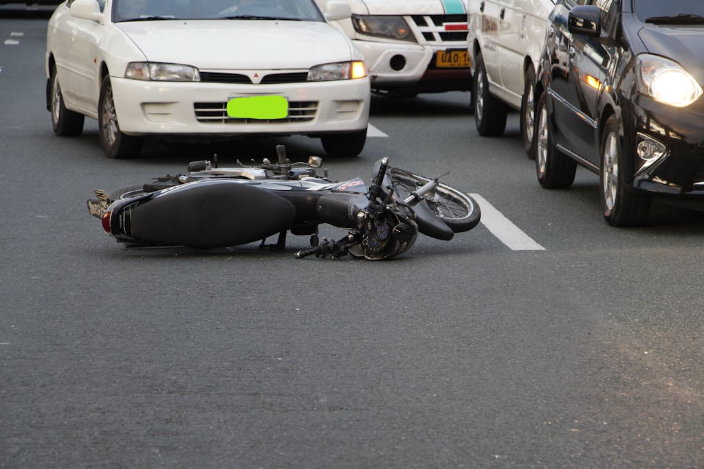 A motorcycle lies on a city road amidst traffic, indicating a recent accident.