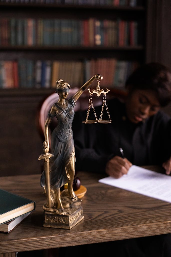 Close-up of Lady Justice figurine on a lawyer's desk with books and documents.